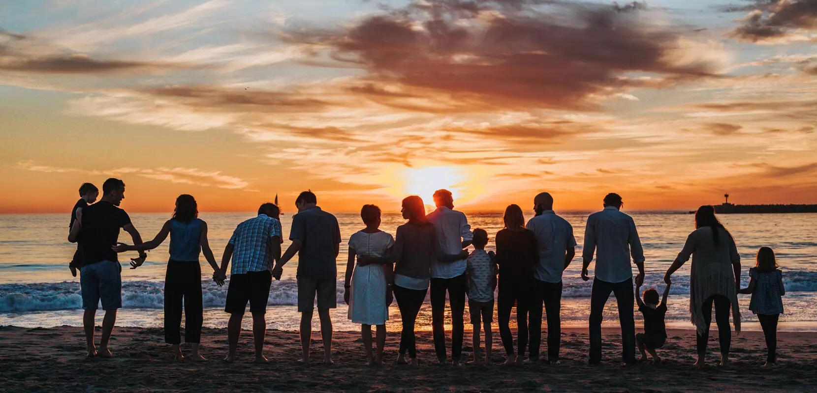 a community of multigenerational people standing on a beach together at sunset