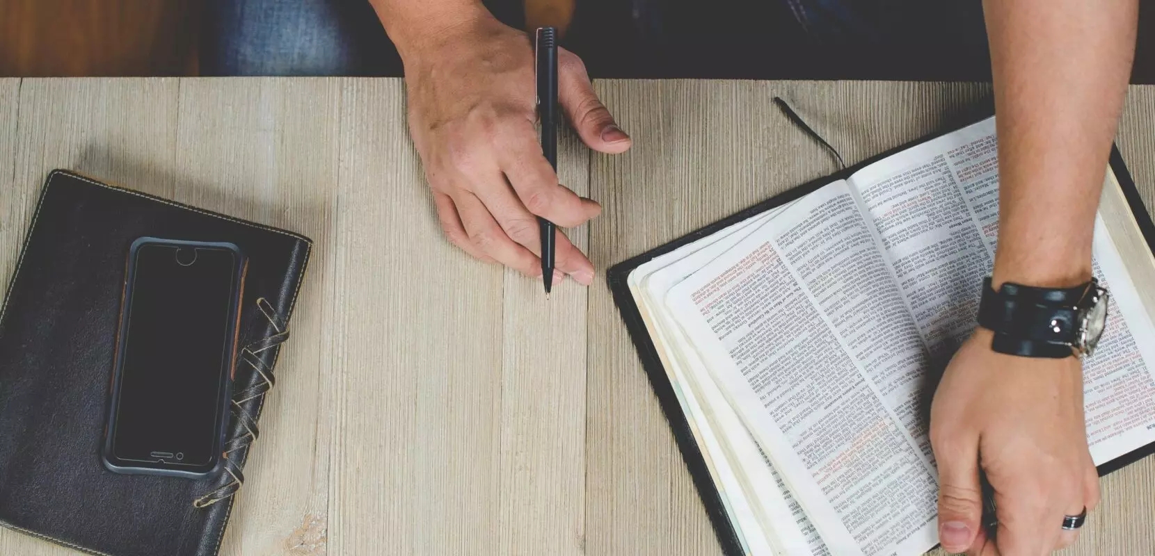 a man sits at his desk reading his bible with a pen in hand to take notes
