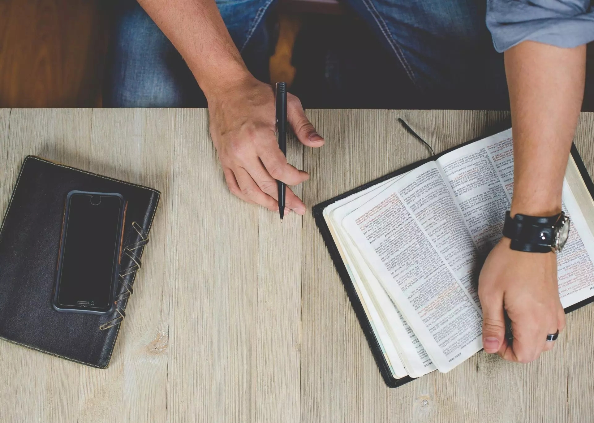 a man sits at his desk reading his bible with a pen in hand to take notes