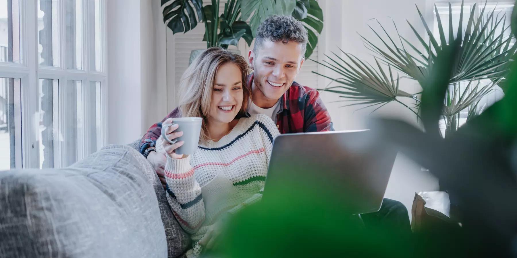 Young couple sitting on couch with coffee looking at their computer reading a newsletter
